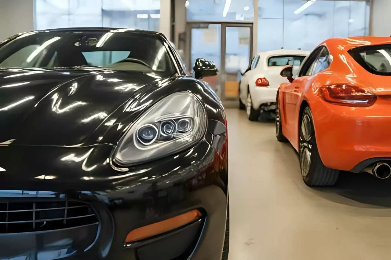 Deretan mobil sport dengan finishing cat mobil Foxapaint warna hitam, putih, dan oranye mengkilap di dalam bengkel pengecatan.