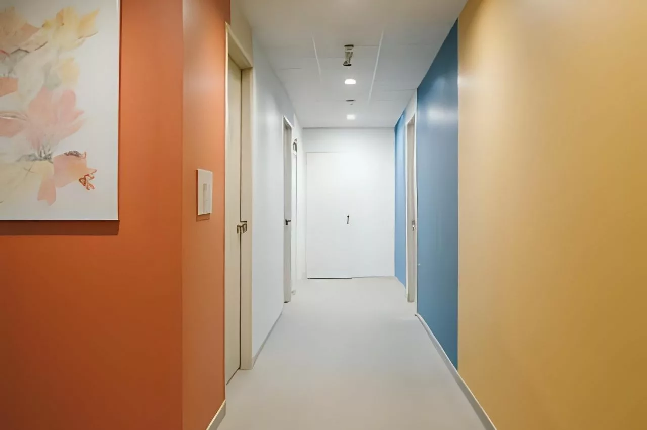 Lorong modern dengan dinding dicat menggunakan warna-warna cerah dari cat tembok Foxapaint, termasuk oranye, biru, putih, dan krem.