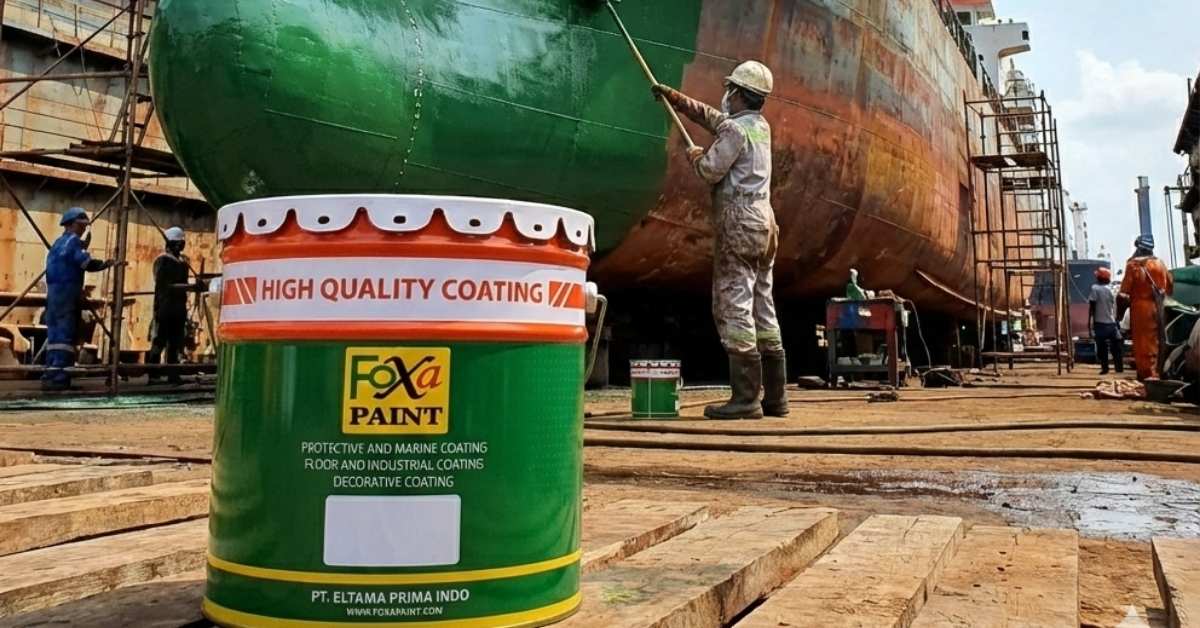 Pekerja melakukan pengecatan lambung kapal di galangan kapal menggunakan cat pelindung Foxapaint, dengan kaleng cat Foxapaint di foreground sebagai coating anti karat dan marine coating berkualitas tinggi.